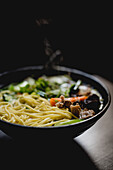 Schüssel mit herzhafter asiatischer Suppe mit Nudeln vor dunklem Hintergrund in einem Cafe