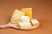 Pieces of assorted fresh cheese placed on wooden chopping board against brown background