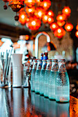 Glasflaschen mit kaltem, erfrischendem Wasser stehen in einer Reihe auf einem Holztresen in einer Bar