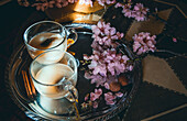 Blick von oben auf Glastassen voller Tee mit Milch, serviert auf einem Tablett mit Zimtstangen und Blumenzweigen in einem Raum mit Sonnenstrahlen