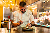 Bearded professional male chef preparing ingredient for sea urchin on plate at table in modern restaurant