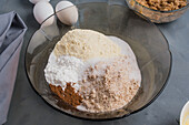 Blick von oben auf eine Glasschale mit verschiedenen Zutaten für gesunde Keto-Kaffee-Muffins mit Mehl auf einem Tisch in einer hellen Küche