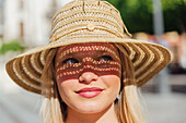 Seitenansicht einer charmanten Frau mit Strohhut, die an einem sonnigen Tag auf einer Straße in einer Stadt im Sommer wegschaut