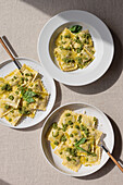 Top view of appetizing cooked ravioli pasta with green sauce and herbs placed on white plates with forks on table