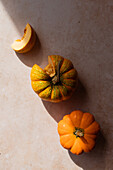 From above of ripe whole pumpkins with cite slice placed in row on beige marble table on sunny day in kitchen
