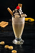 Glas süßer Bananenmilchshake, garniert mit Schlagsahne, Waffeln und Kirsche mit Schokolade obenauf