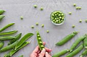 From above of cropped unrecognizable person hands peeling green pea pods on table at home