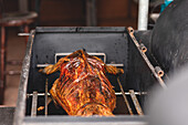 Delicious cut roasted suckling lamb with ribs hanging on metal grid in barbecue grill in light cafe during cooking process