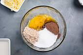 Blick von oben auf eine Glasschale mit Zutaten für süße Schokoladenwaffeln mit Rohrzucker und Kakao auf grauem Hintergrund in der Küche