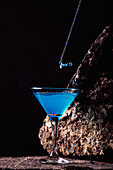 Tropfen eines blauen Lagunencocktails in einem eleganten Kristallglas auf einer rauen Oberfläche vor einem schwarzen Hintergrund