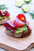 Tasty appetizers of rye bread toasts with avocado spread and smoked salmon slices with dill sprigs on chopping board