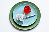 Draufsicht auf appetitliches rotes Beerengelee auf einem hellblauen runden Teller mit einem Joghurtbecher mit Löffel auf weißer Fläche