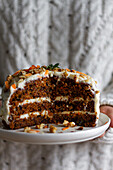 Crop anonymous cook holding plate with tasty cake with cream cheese and moist biscuit decorated with crushed nuts and carrot slices