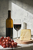 Arrangement aus aromatischem Rotwein im Glas, serviert auf dem Tisch neben Weinflasche, reifen Trauben und dreieckigem Käsestück