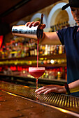 Young Asian bartender working in the bar with his shaker and pouring a cocktail in the glass