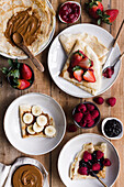 From above plates of tasty crepes with assorted toppings placed on lumber table during breakfast