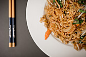 From above composition of plate with beef vegetable noodles and chopsticks placed on grey table
