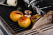 Nahaufnahme rohe Scheiben frischer Tomaten und Knoblauchköpfe beim Grillen auf einem Metallrost