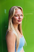 Seitenansicht einer koketten Frau mit blondem Haar, die der Kamera auf grünem Hintergrund zuzwinkert