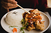 Frau sitzt in einem asiatischen Café und isst appetitlich gewürzte Ente mit Reis