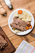 Blick von oben auf schmackhafte, appetitanregende Scheiben von gewürztem Corned Beef mit Kohl und Karotten, serviert auf einem Teller auf einem Holztisch