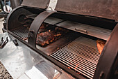 Tasty pork ribs with fried crust grilling in metal barbecue with racks and opened lids placed on surface in cafe