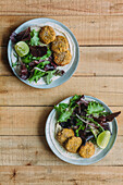 Plates with fresh lettuce salad and sweet potato falafel near sauce and sesame on wooden table