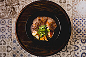 Von oben dunkle Schüssel mit schönen Portion Rindfleisch Gemüse auf Holztablett platziert
