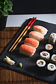 Appetizing sushi rolls with fish served on black board near chopsticks and wasabi