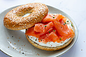 From above fresh bagel with cheese and salmon on plate served on table in light kitchen