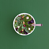 Blick von oben auf einen leckeren Salat mit Spinat, Bohnen und Walnüssen, der in einer Schüssel auf einem Holztisch für ein gesundes Mittagessen serviert wird