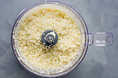 Draufsicht auf rohen, gesunden, zerkleinerten weißen Blumenkohl in einem modernen Mixer auf dem Tisch während des Kochvorgangs in einer hellen Küche