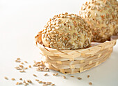 High angle of freshly baked buns with sunflower seeds served in wicker bowl on white background