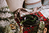 Christmas table setting with wreath on ceramic plate on red checkered tablecloth on the background with lights