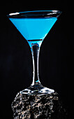 Blaue-Lagune-Cocktail in elegantem Kristallglas auf rauer Oberfläche vor schwarzem Hintergrund
