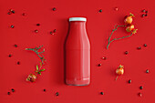 From above bottle of fresh juice of red color placed on dark red background with pomegranate seeds and small pomegranates in branch