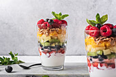 Appetizing yogurt with layers of fresh fruits served in glasses on table with mint leaves