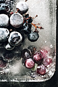 Draufsicht auf ein Stück Eis mit Weintrauben auf einem Metalltablett im Sonnenlicht
