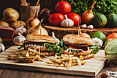 Appetizing hamburgers with vegetables and cutlets placed on wooden board with French fries in kitchen