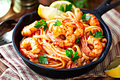 From above spaghetti with shrimps or prawns in tomato sauce garnished with parsley and wedges of lemon