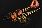 Hand holding delicious cooked spicy skewers with meat and healthy broccoli