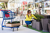 Content female customer picking pots or green plants during shopping in spacious garden center