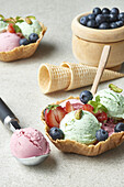 High angle of delicious homemade pistachio and strawberry ice cream scoops served in waffle bowl and decorated with fresh berries in daylight