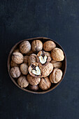 Round shaped wooden bowl full of crunchy walnuts with dry uneven nutshells on table