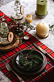 Draufsicht auf einen weihnachtlich gedeckten Tisch mit Kranz auf dem Teller, dekorativem Holzschmuck und rot-karierter Tischdecke mit gelben Lichtern im Hintergrund