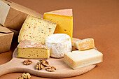 Pieces of assorted fresh cheese placed on wooden chopping board against brown background