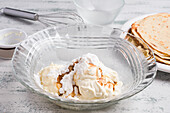 Produkte für Keto-Diät-Crepes mit Frischkäse-Vanille und Erythrit-Süßstoff in Glasschüssel auf dem Tisch mit Schneebesen