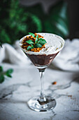 Glass of sweet mousse with chocolate and coconut garnished with mint leaves and placed on table with green plants