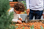 Abgeschnittener, nicht erkennbarer Teenager, der seinem Bruder zeigt, wie man mit einer Schaufel gärtnert, während er im Garten auf dem Land arbeitet