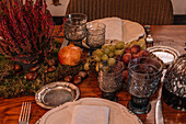 High angle of crystal glasses near plate and cutlery placed on table decorated with grapes Calluna vulgaris flowers and pomegranate